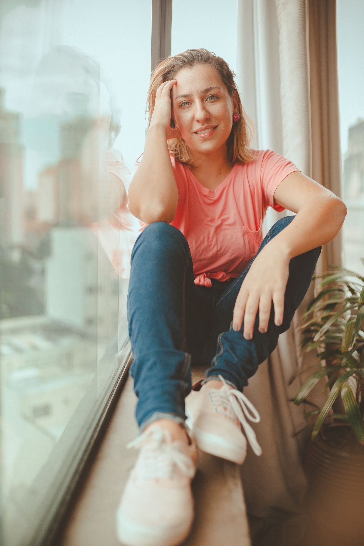 A relaxed woman in casual attire enjoys a quiet moment on a windowsill indoors.