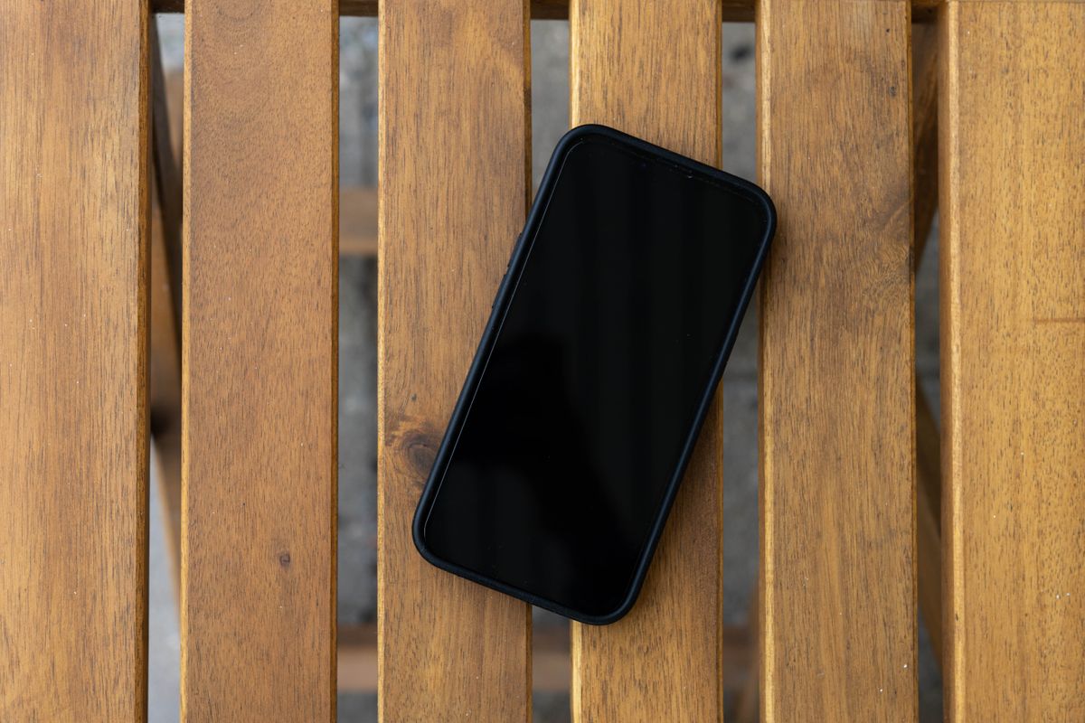 A smartphone with a black screen lies on a wooden slatted table, viewed from above.