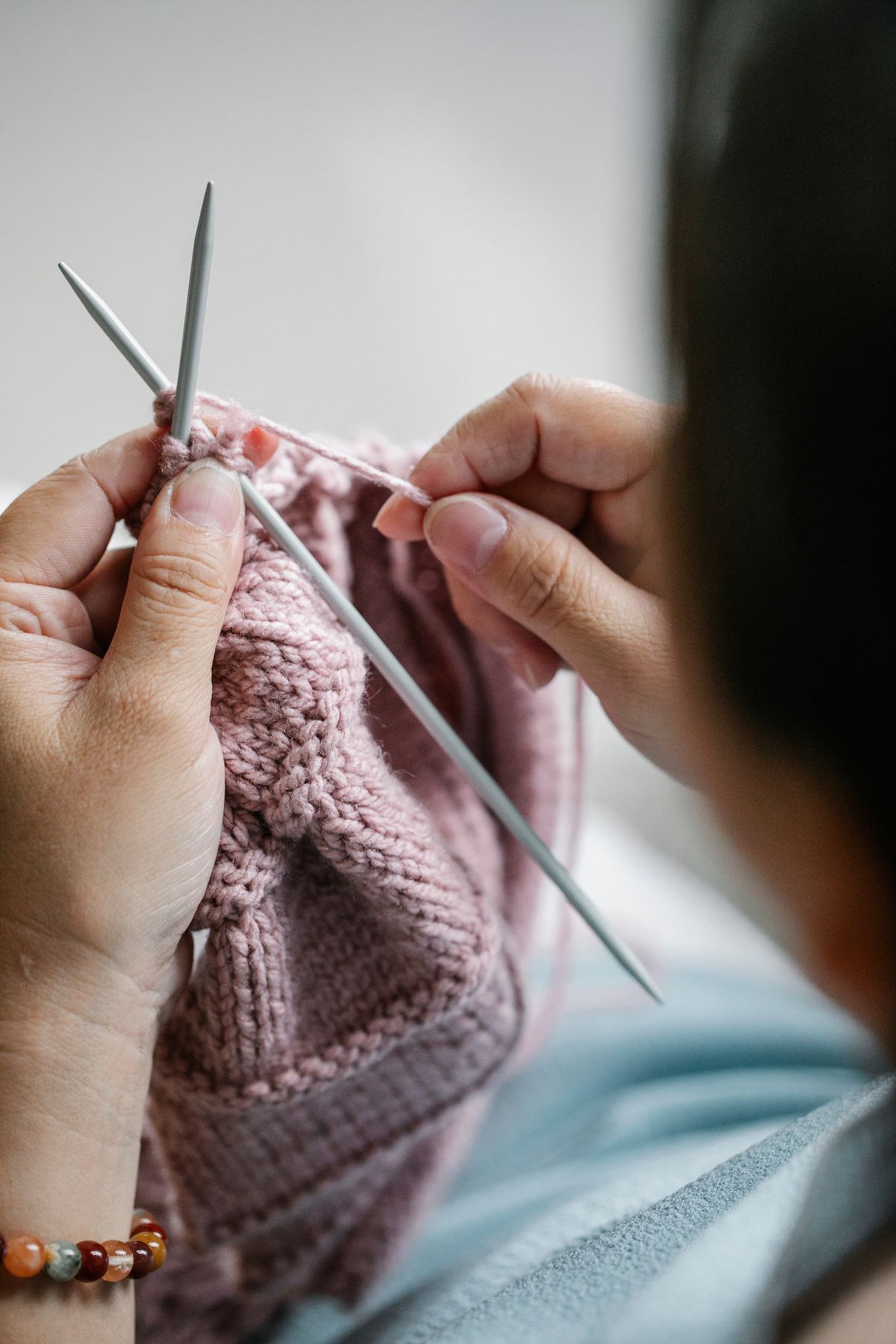 From above faceless woman with knitting needles and pink yarn thread knitting at home