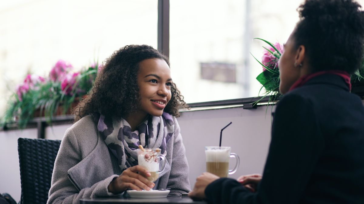 Two women chatting over coffee at a cozy café with flowers in the background.